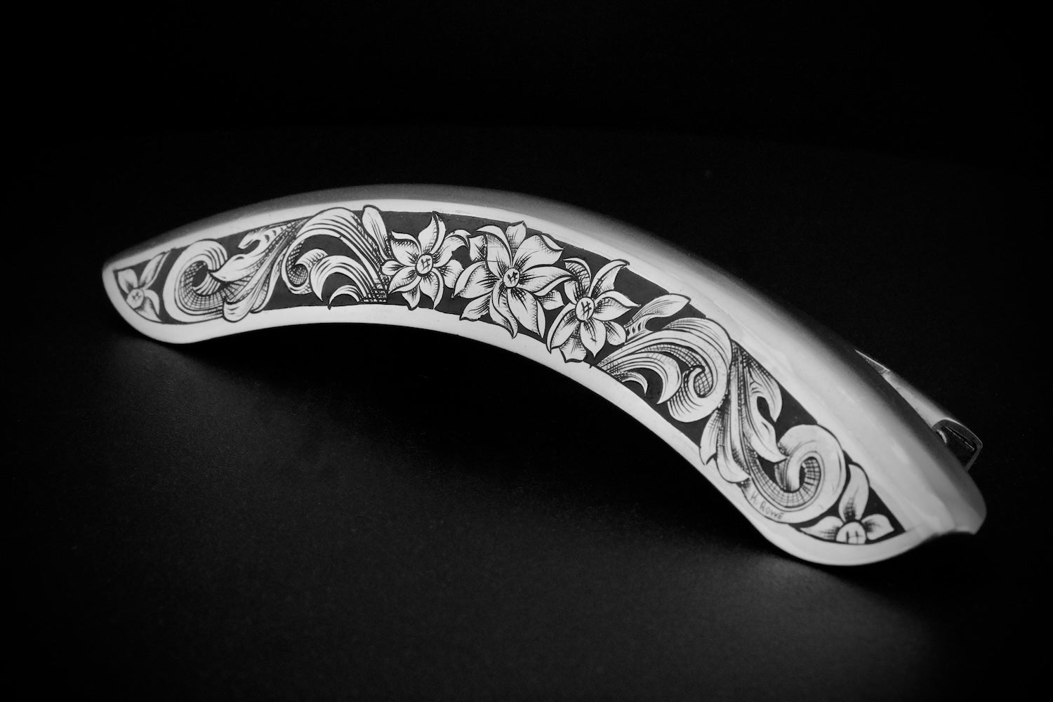 hand engraved metal banjo armrest with floral patterns on a black background