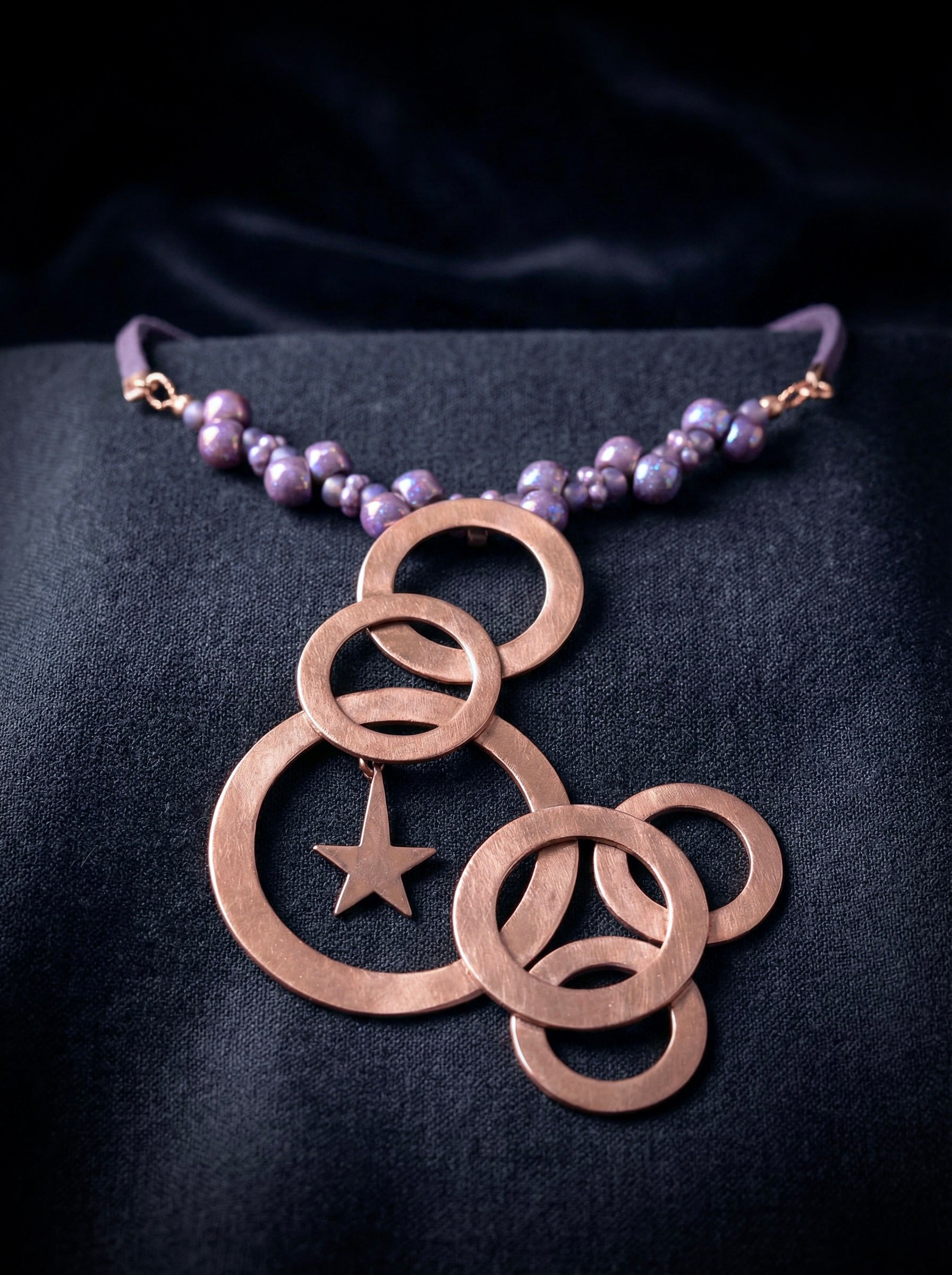 Bronze necklace with circular pendants and a star on a dark fabric background