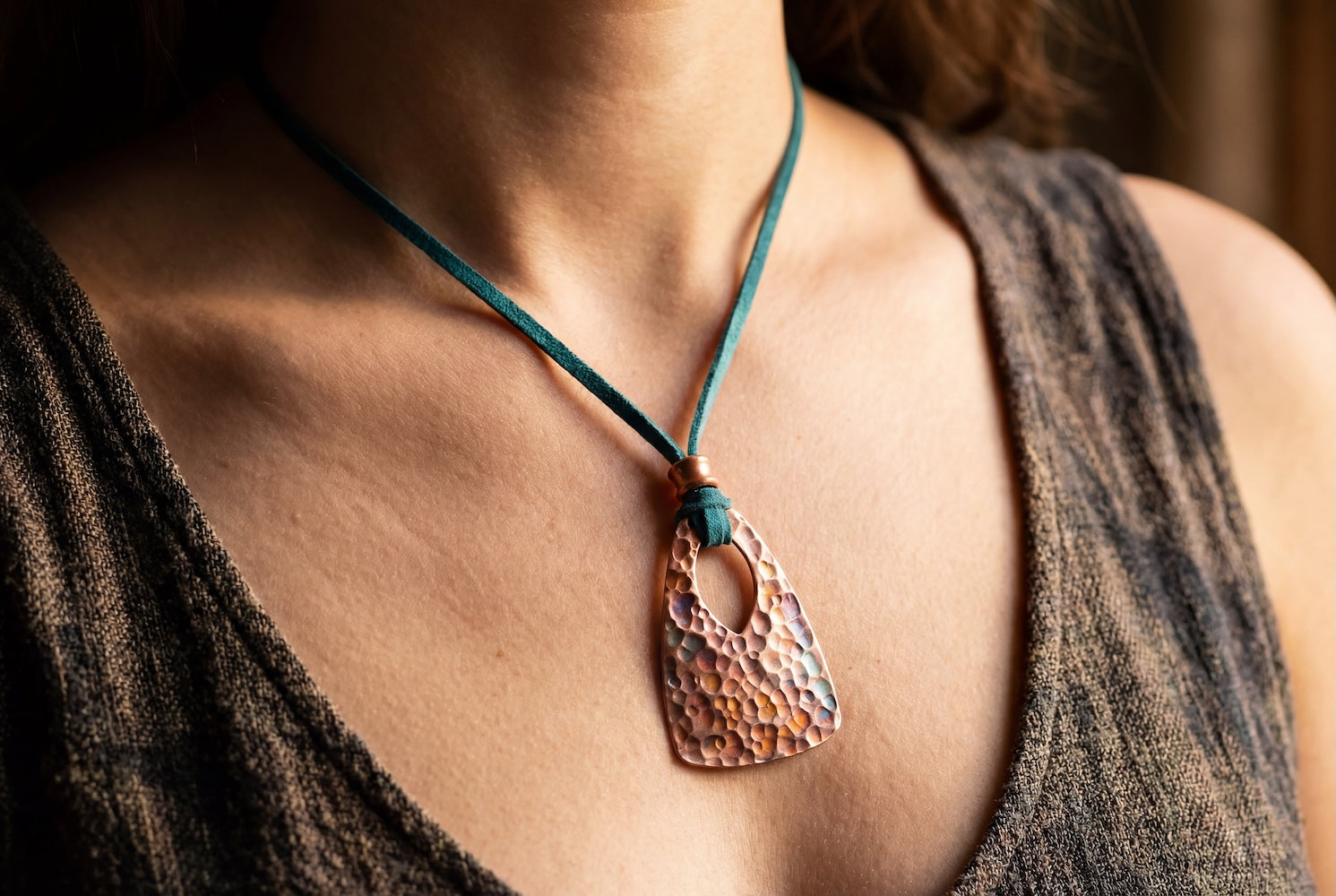 Close-up of a person wearing a copper pendant necklace with a textured design.