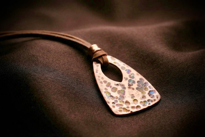 Metallic pendant with a textured surface on a brown leather strap against a dark background