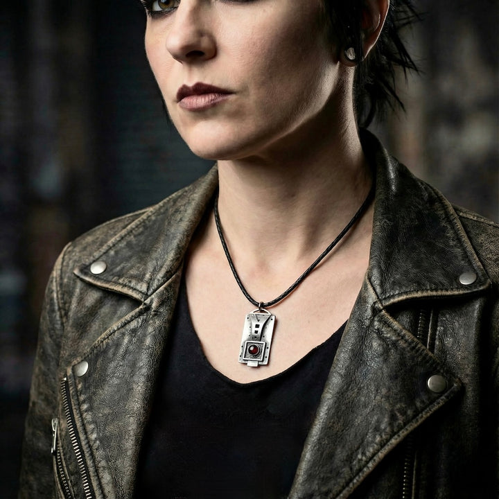 Person wearing a leather jacket and necklace with a silver pendant, against a dark background
