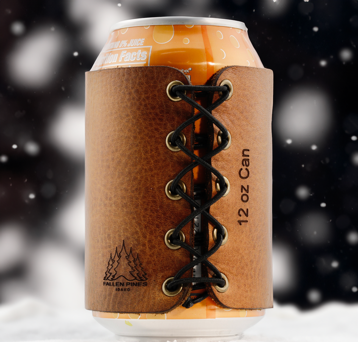 Brown leather can cooler with lace-up design holding a 12 oz can against a blurred snowy background