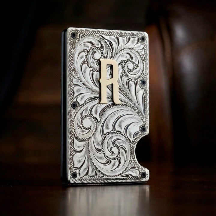 Decorative metal wallet with intricate patterns and a brass letter 'A' on a dark background