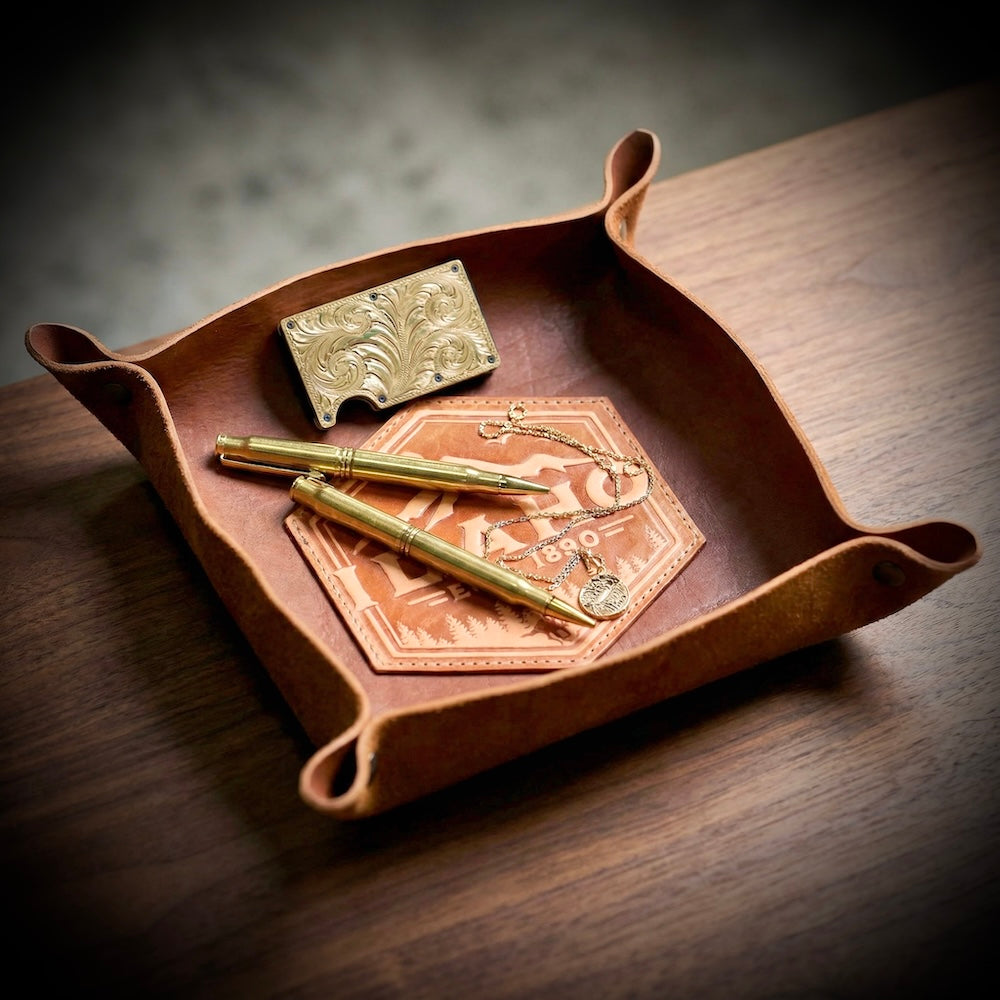 Brown leather tray with gold items on a wooden surface