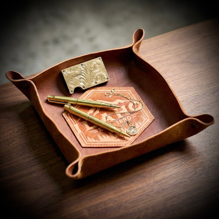 Brown leather tray with gold items on a wooden surface