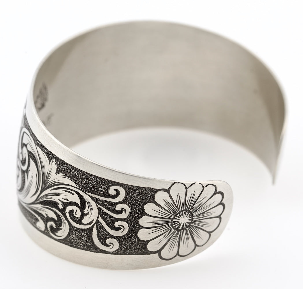 Silver bracelet with floral and scroll designs on a white background