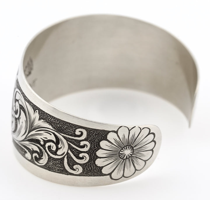Silver bracelet with floral and scroll designs on a white background