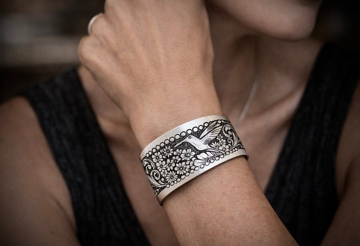 Silver bracelet with intricate design on a wrist against a blurred background