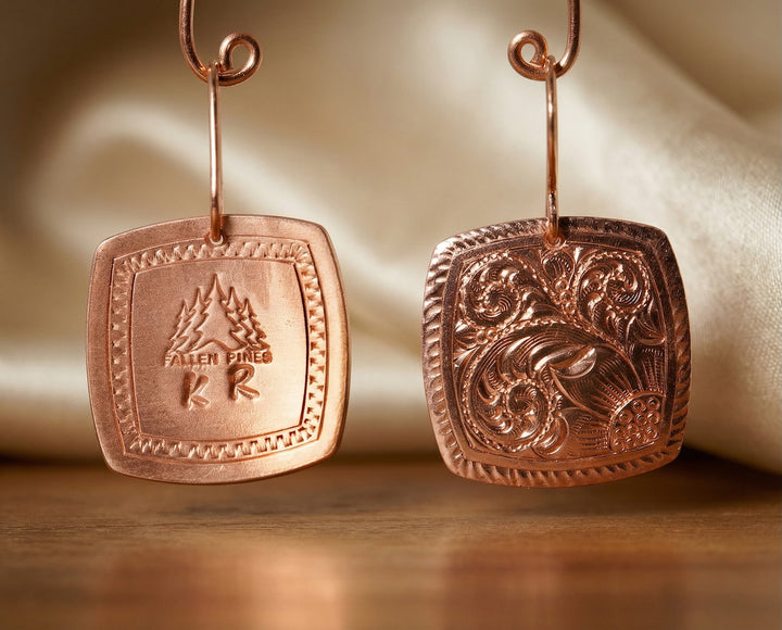Pair of copper earrings with engraved designs on a wooden surface