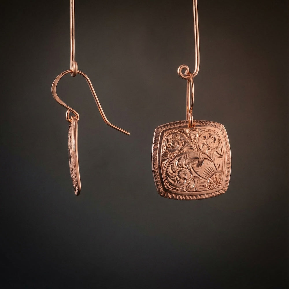 Pair of copper earrings with intricate designs on a dark background
