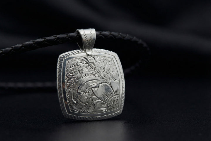 Silver pendant with intricate design on a black background