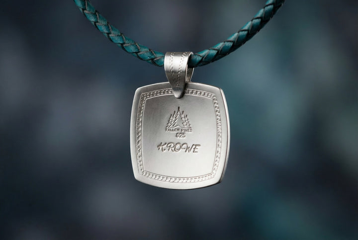 Silver pendant with engraved design on a blurred blue background