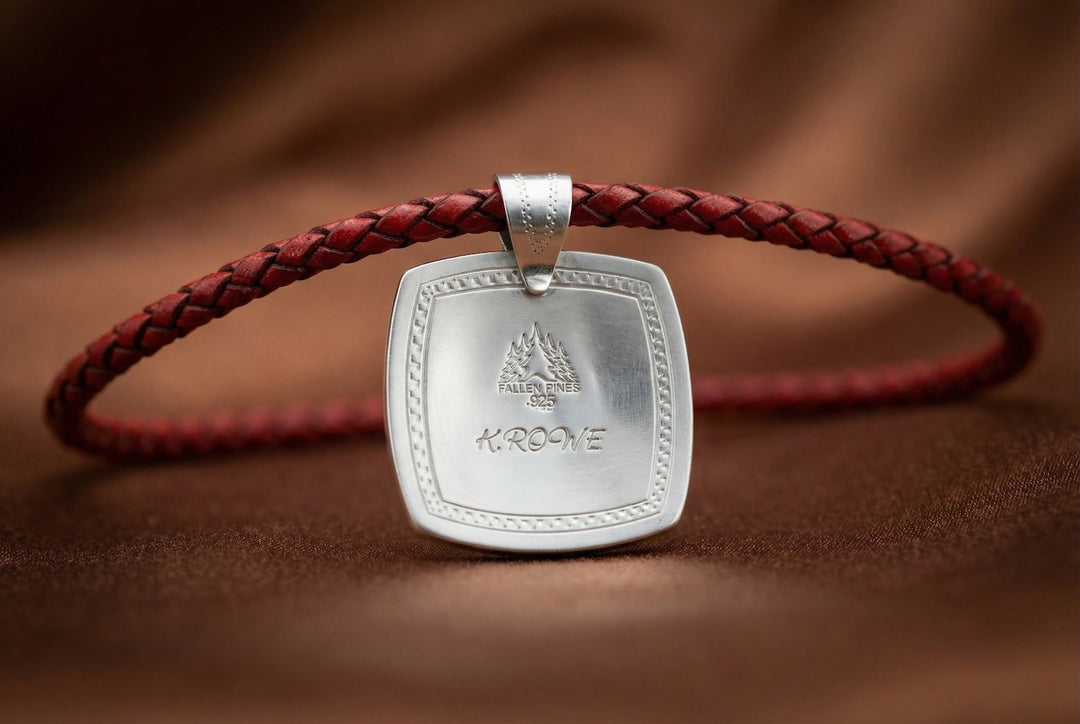 Silver pendant on a braided red cord against a brown background