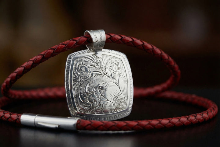 Silver pendant with intricate design on a red leather cord against a dark background