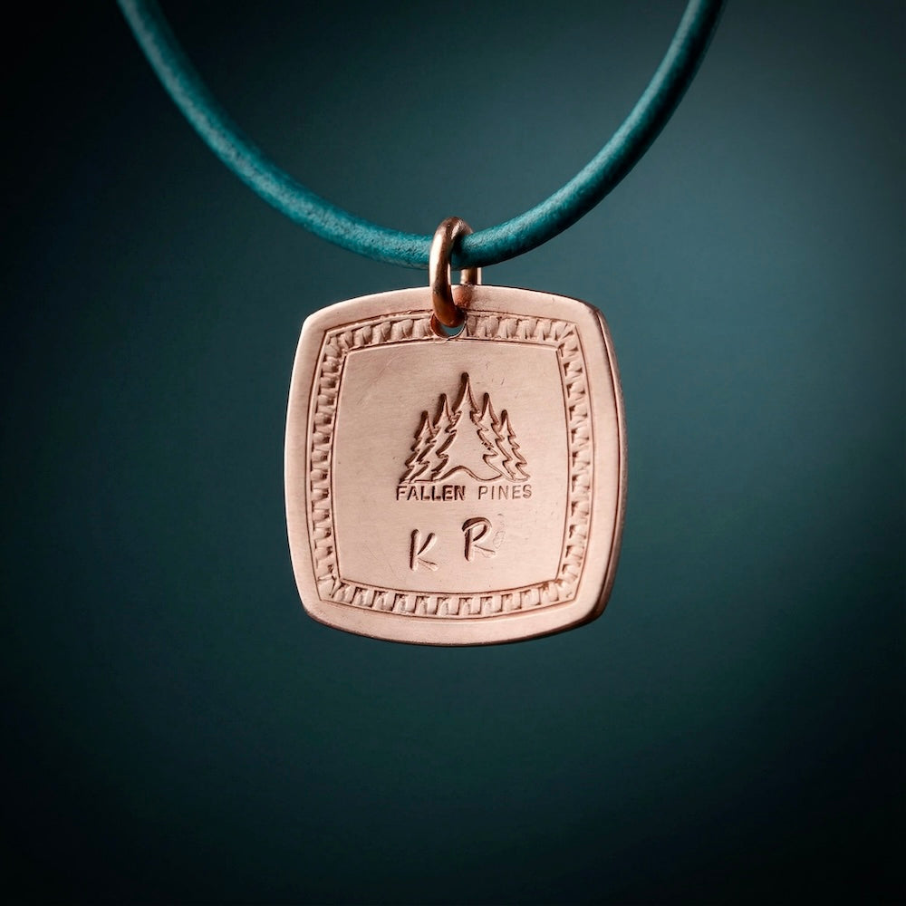 Bronze pendant with engraved design on a teal cord against a dark background