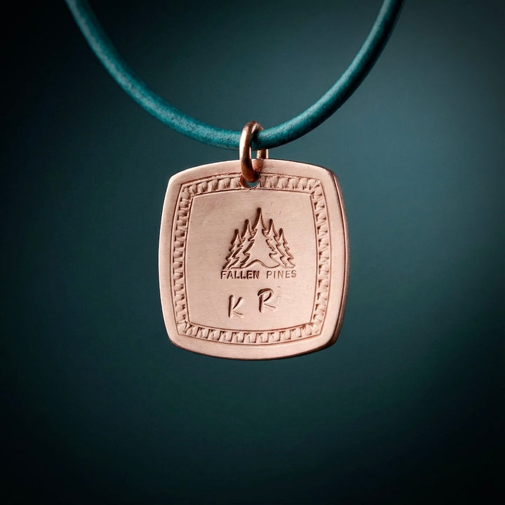 Bronze pendant with engraved design on a teal cord against a dark background
