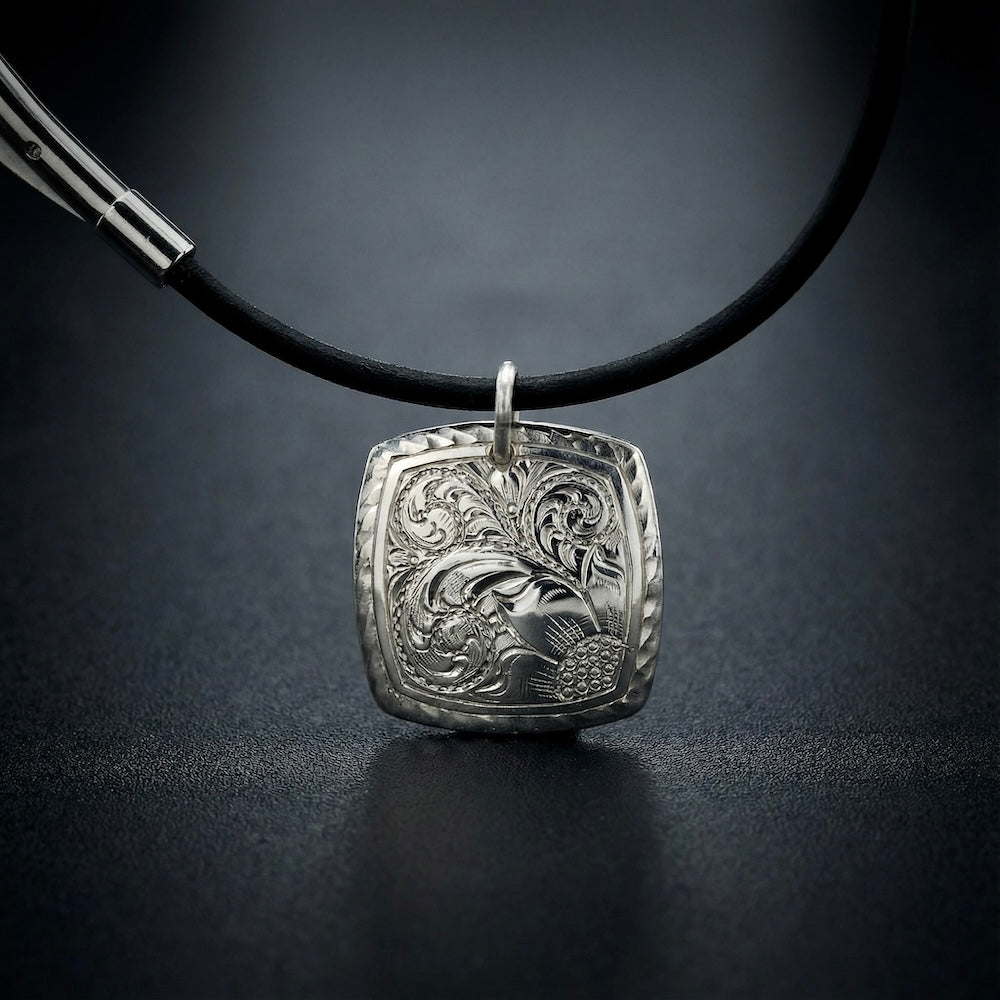 Silver pendant on a black cord against a dark background