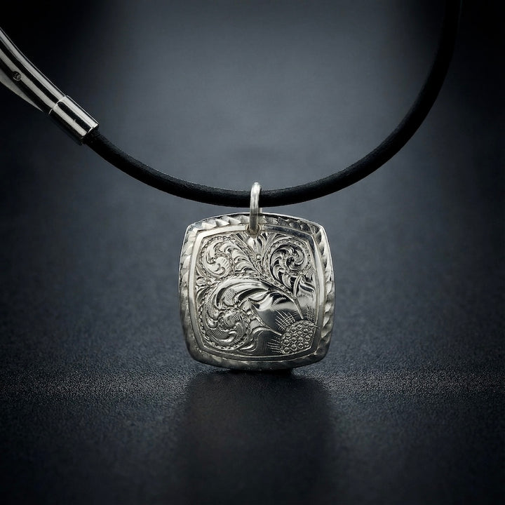 Silver pendant on a black cord against a dark background
