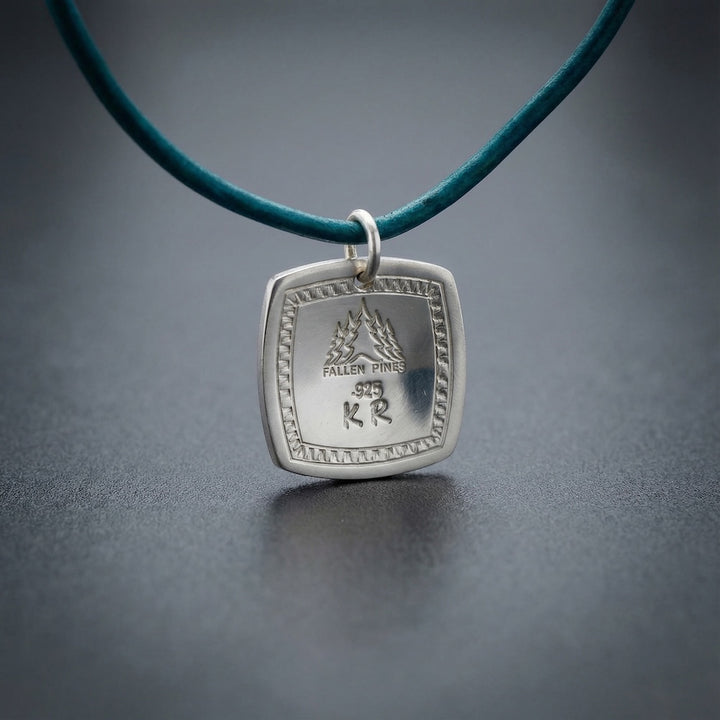 Silver pendant with engraved text on a teal cord against a dark background