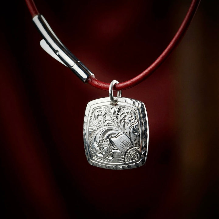 Silver pendant with intricate design on a red cord against a dark background