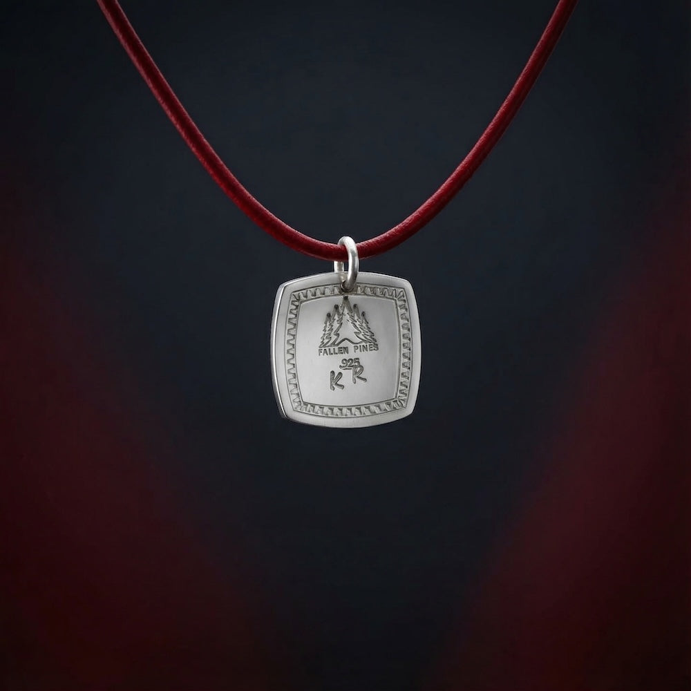 Silver pendant on a red cord against a dark background