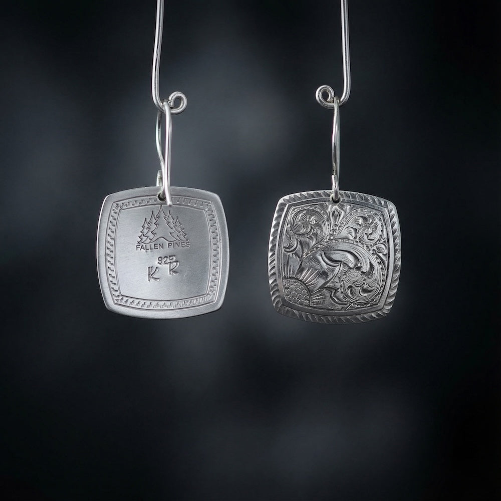 Pair of silver earrings with intricate designs on a dark background