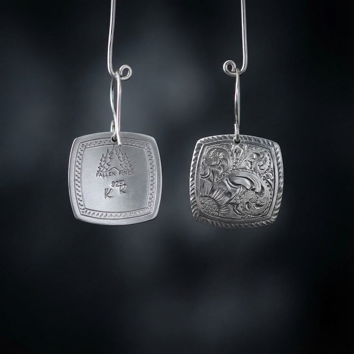 Pair of silver earrings with intricate designs on a dark background